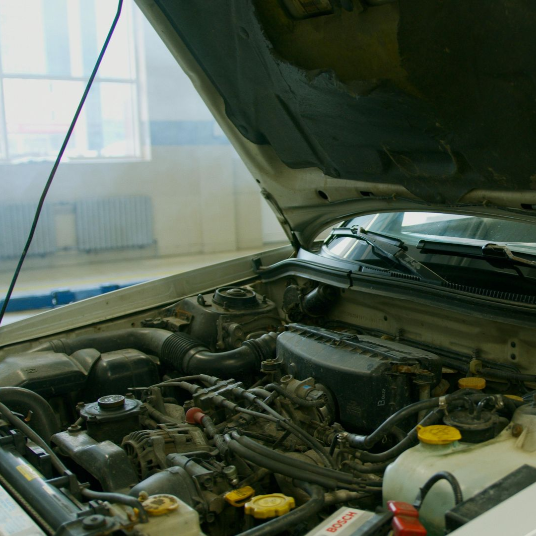 Capó abierto que revela motor y componentes. Coche blanco en garaje.