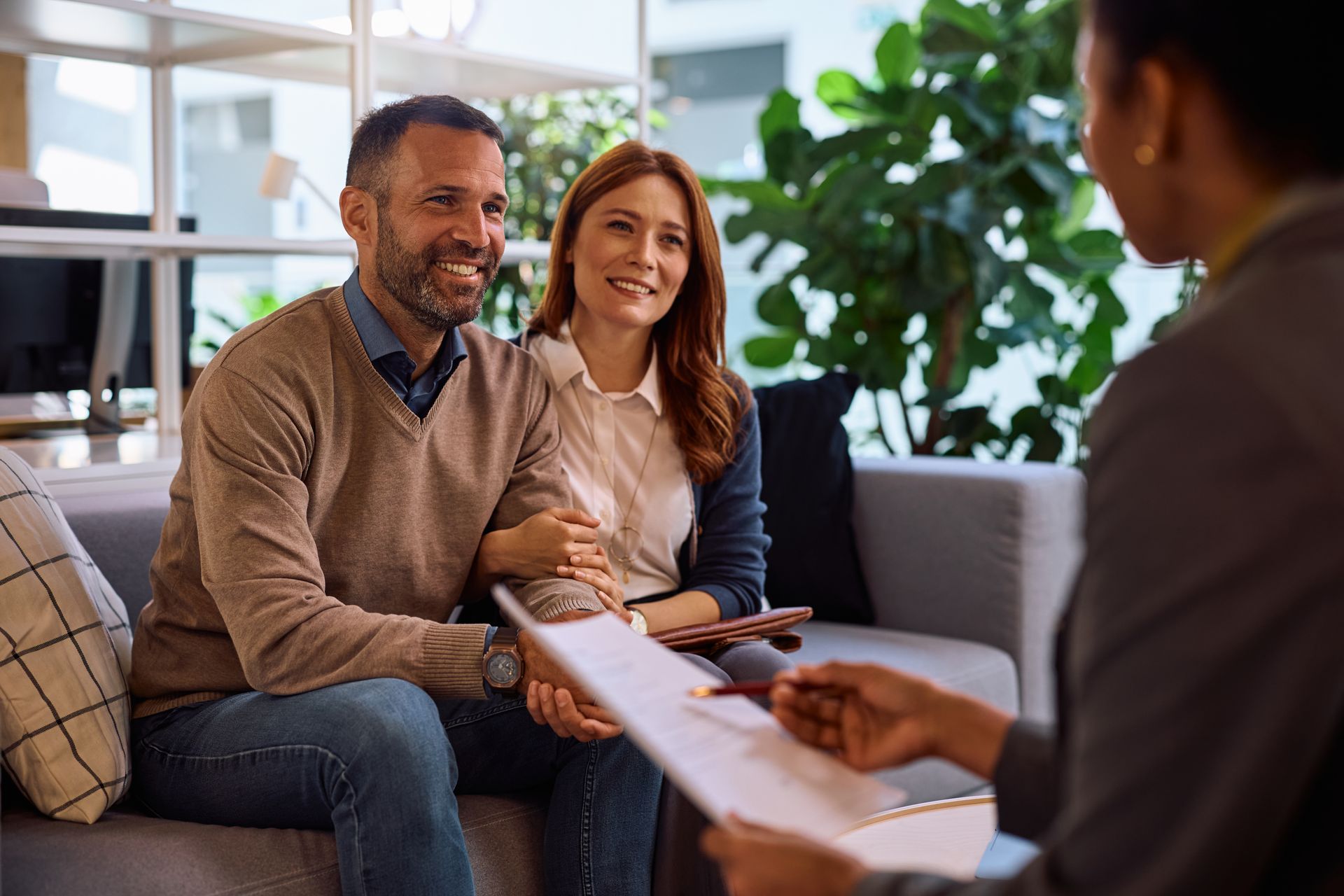 A smiling couple reviews documents with a financial advisor in a bright, modern office setting.
