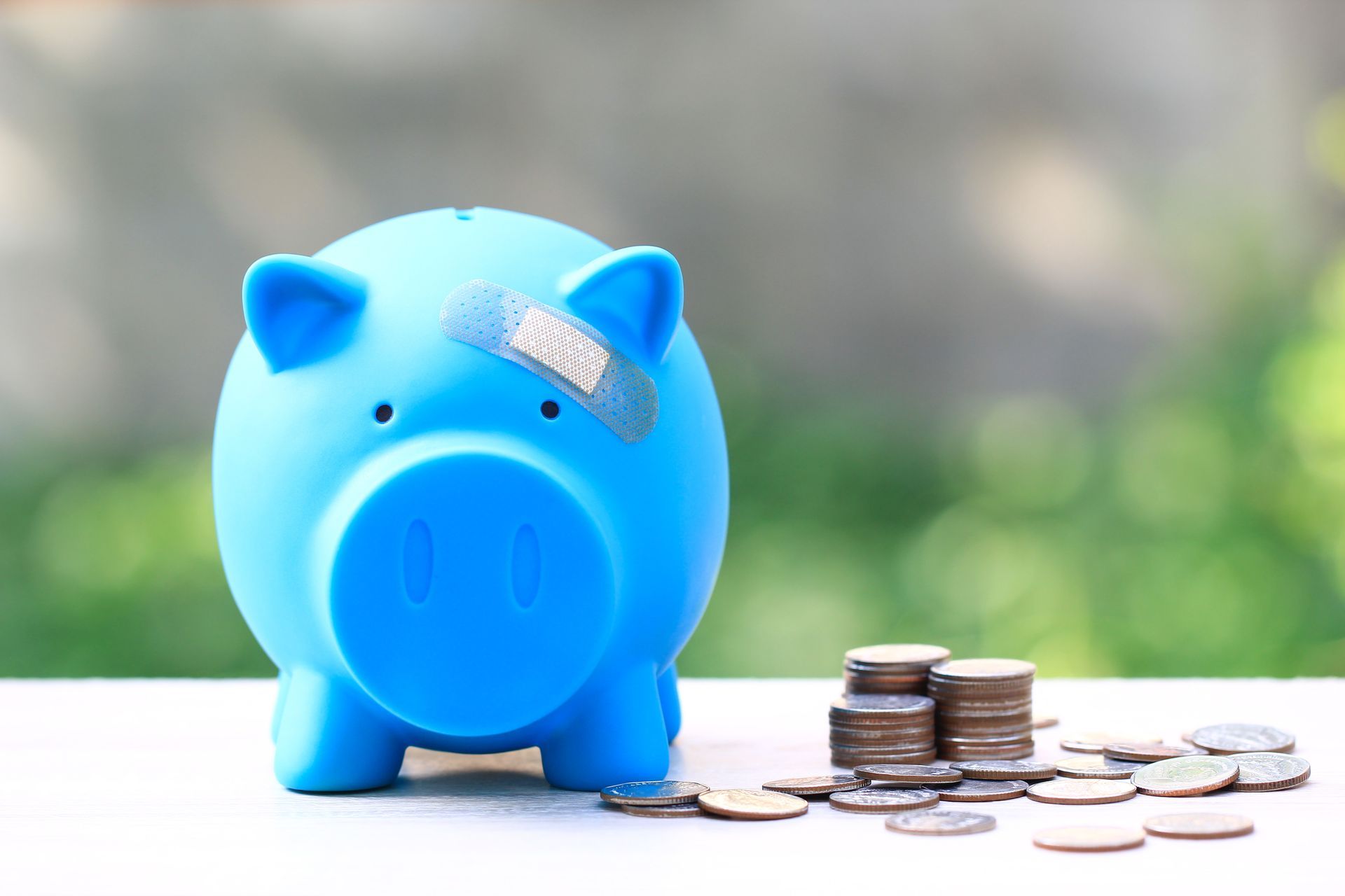 Blue piggy bank with a bandage on its head, sitting next to stacks of coins and scattered change.