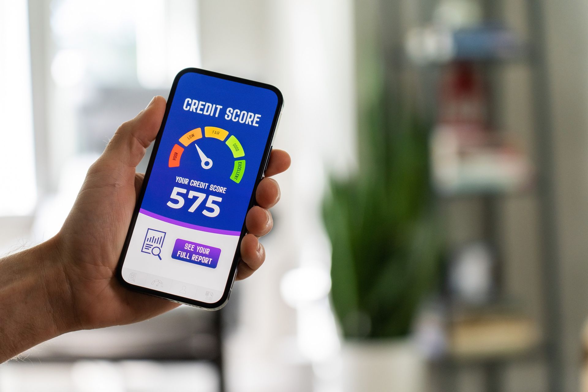 Hand holding a smartphone displaying a credit score of 575, which is considered fair. The score is shown on a colorful gauge.