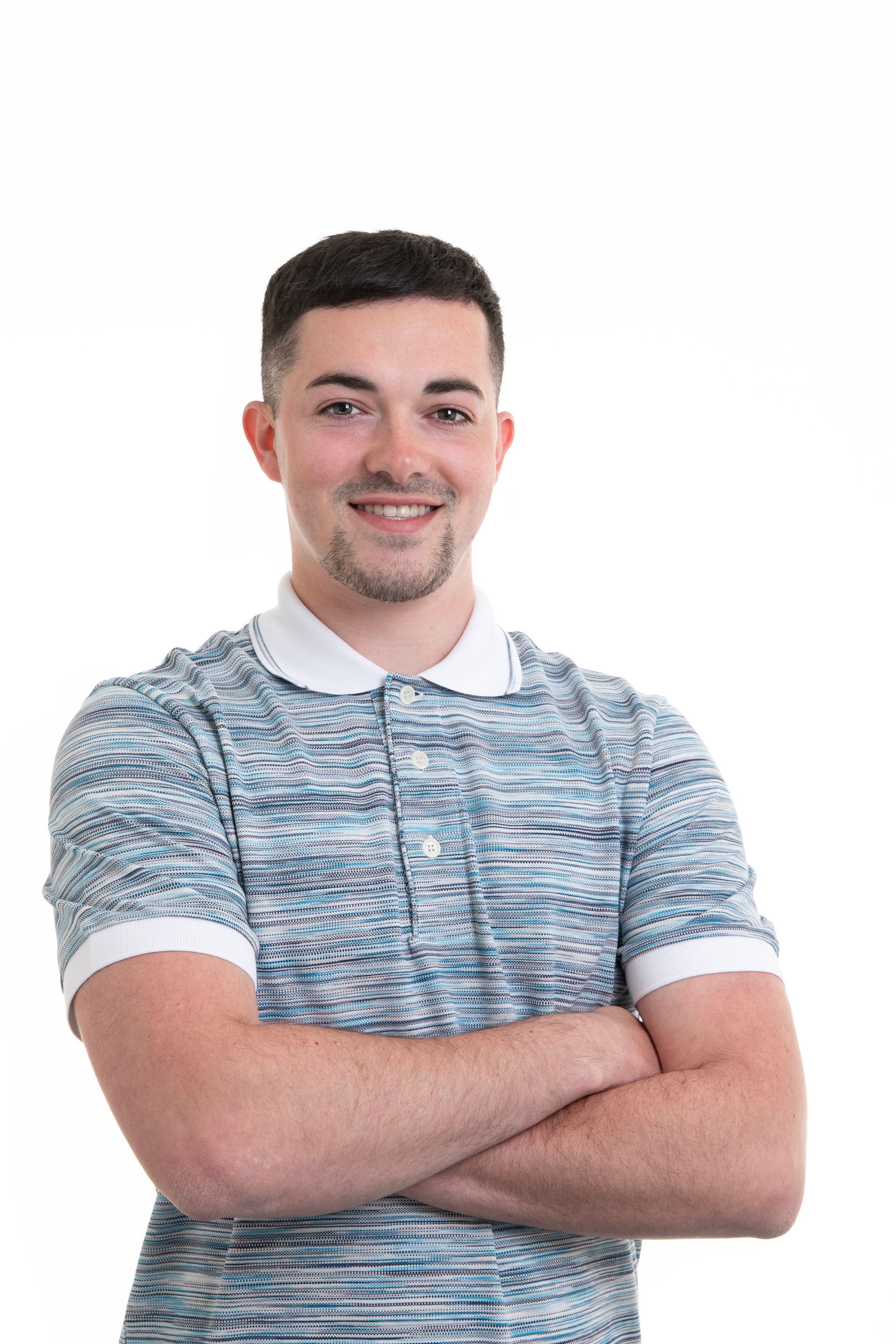 A young man is standing with his arms crossed and smiling.