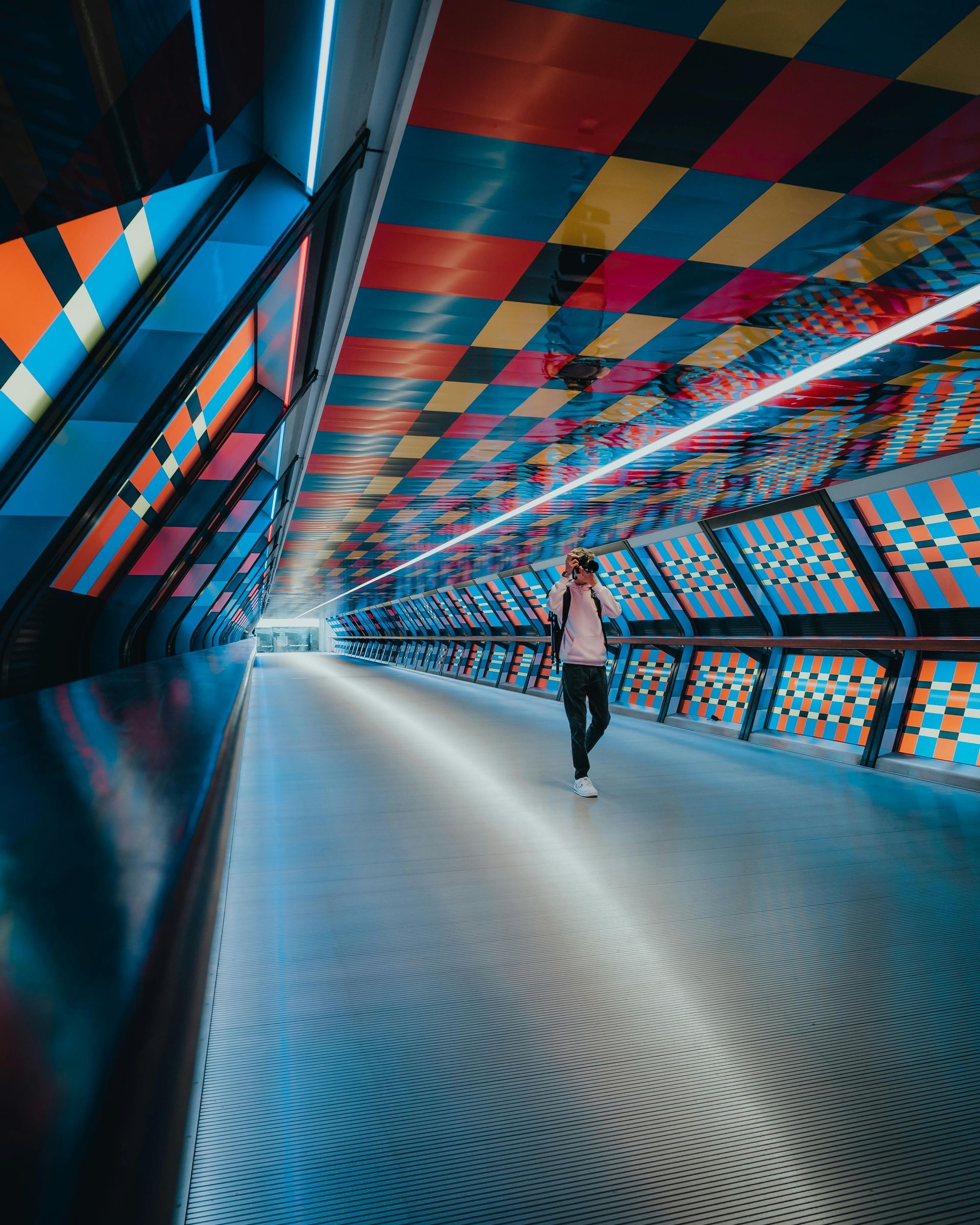 The image shows the Adams Plaza Bridge in Canary Wharf, London, which has been transformed by artist Camille Walala with a colorful geometric design. 