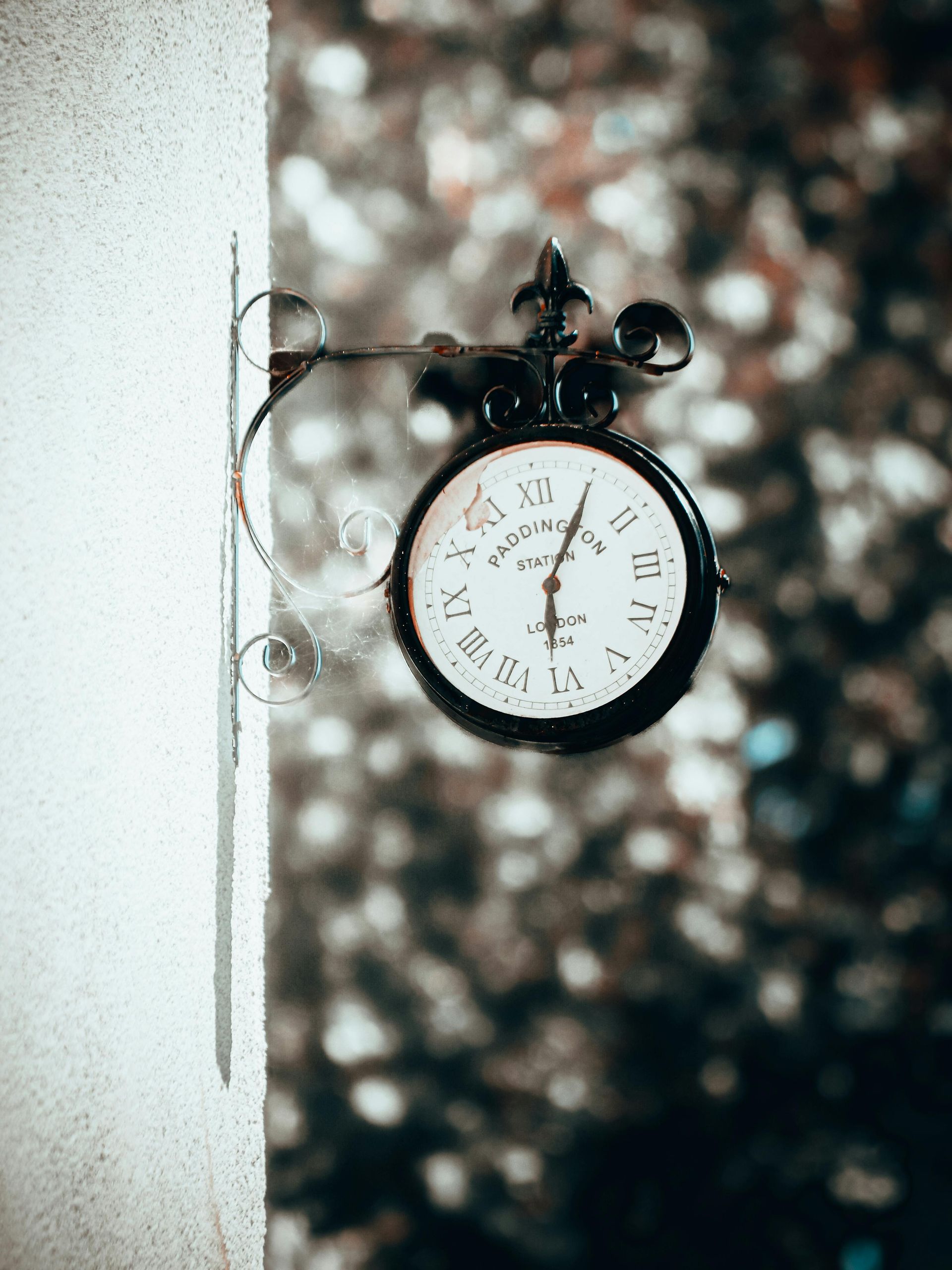 A black and white clock is hanging on a wall with inscription Paddington Station on it.