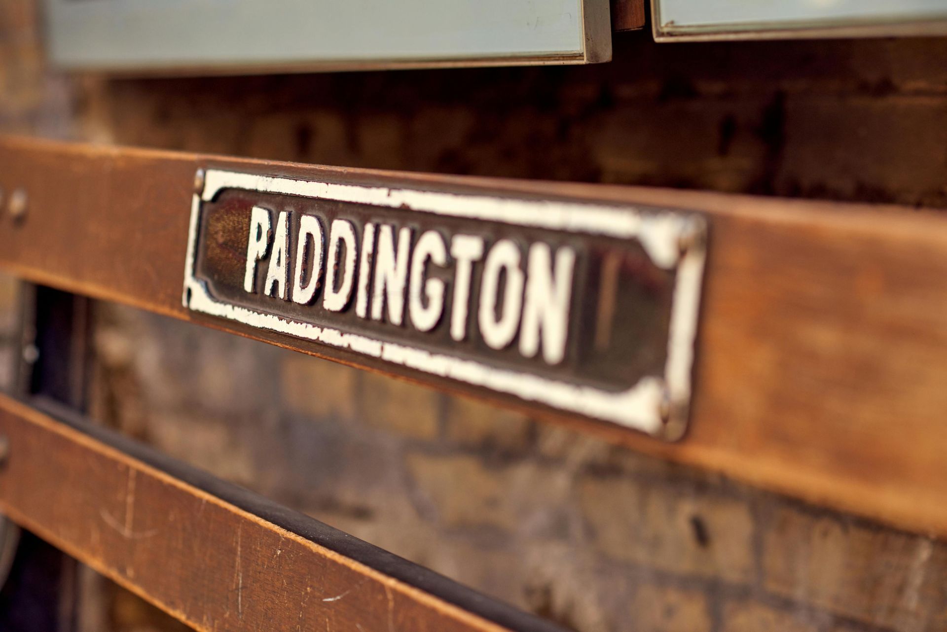 A wooden sign that says paddington is hanging on a brick wall.