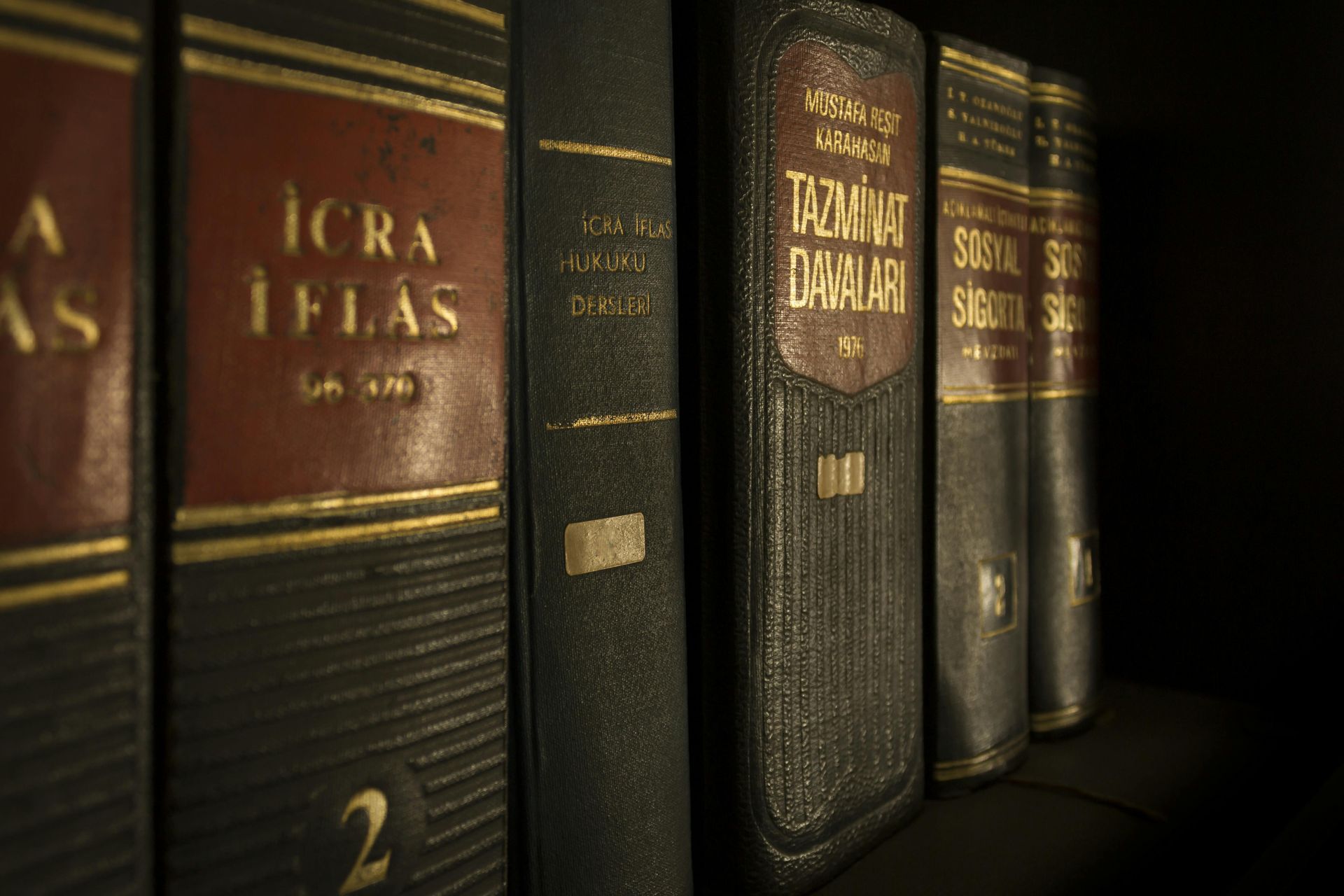 Close-up of dark, leather-bound law books with gold lettering on a shelf. Red and gold accents are visible.