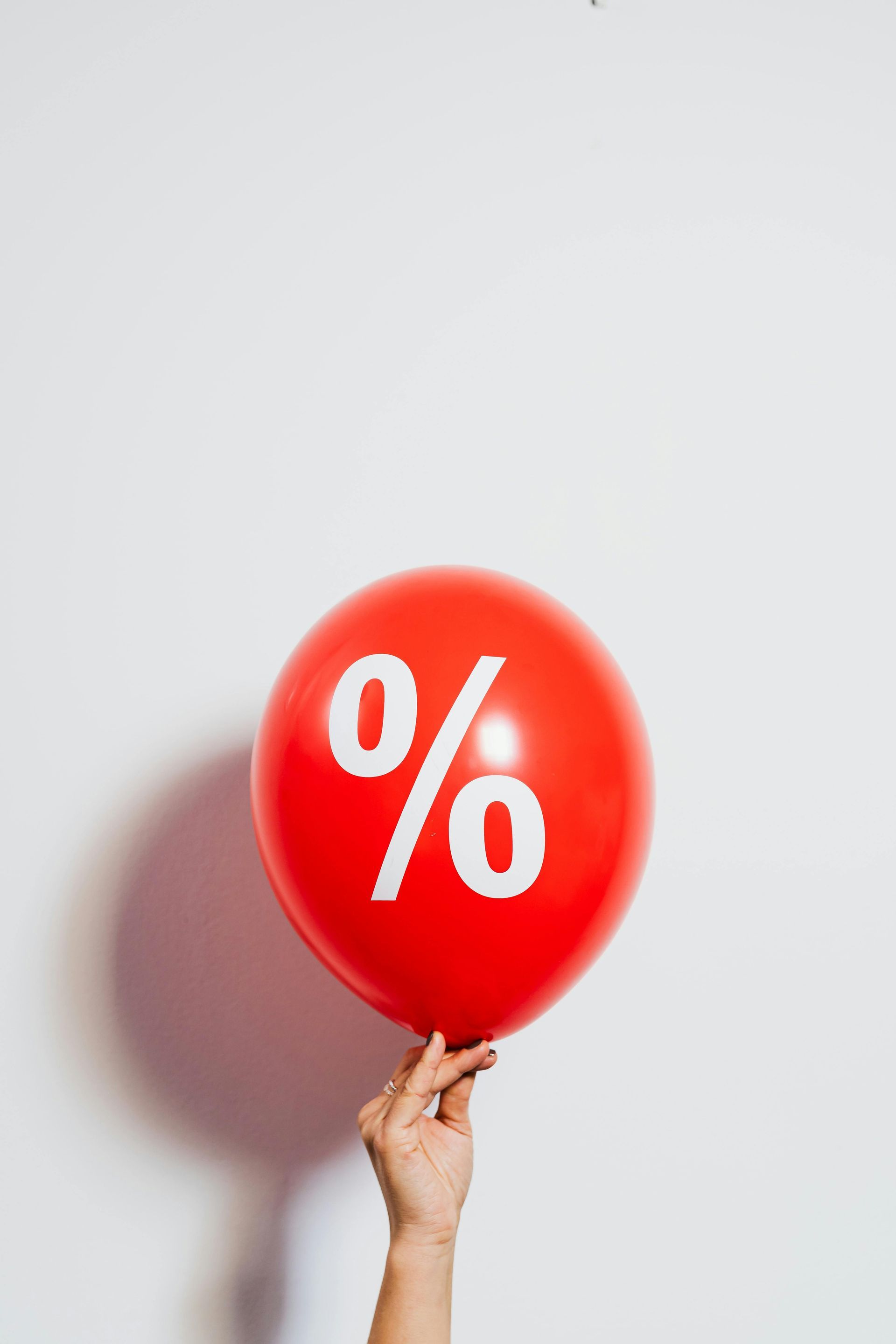 Red balloon with a white percent symbol held by a hand against a white background.