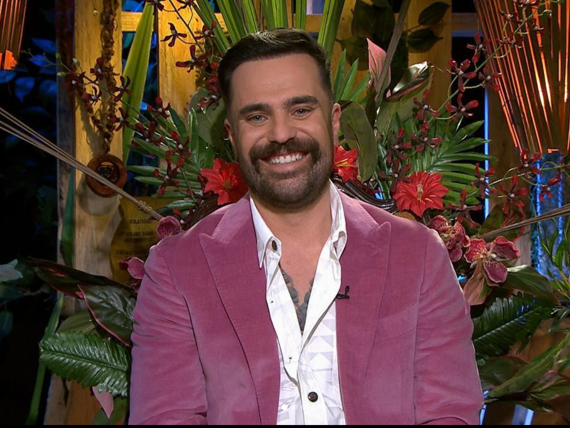 A man in a pink jacket is smiling in front of flowers.
