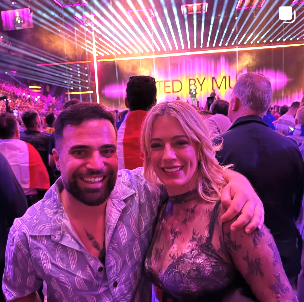 A man and woman are posing for a picture in front of a sign that says ted by mu