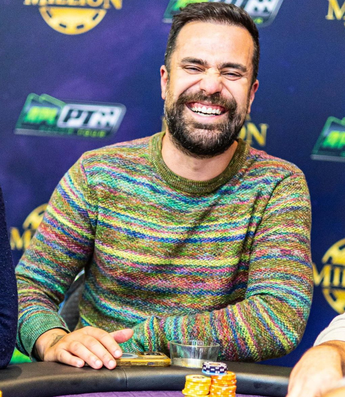 A man with a beard is smiling while sitting at a poker table