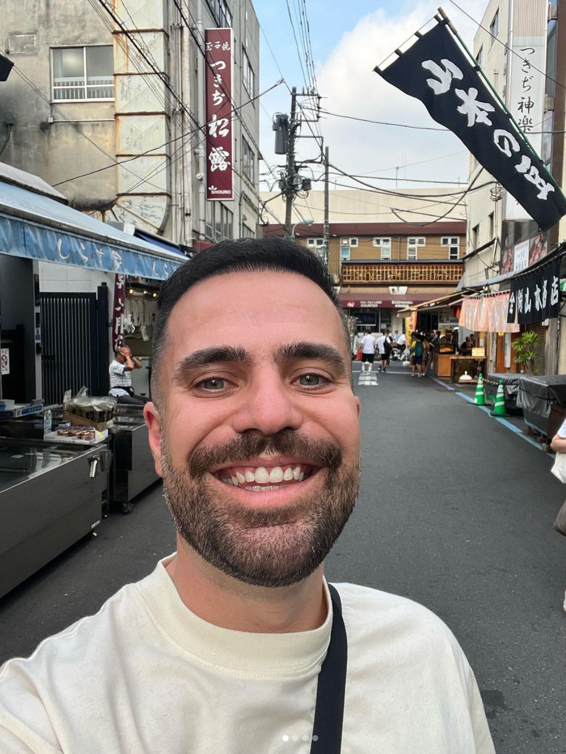 A man with a beard is smiling while taking a selfie on a city street.