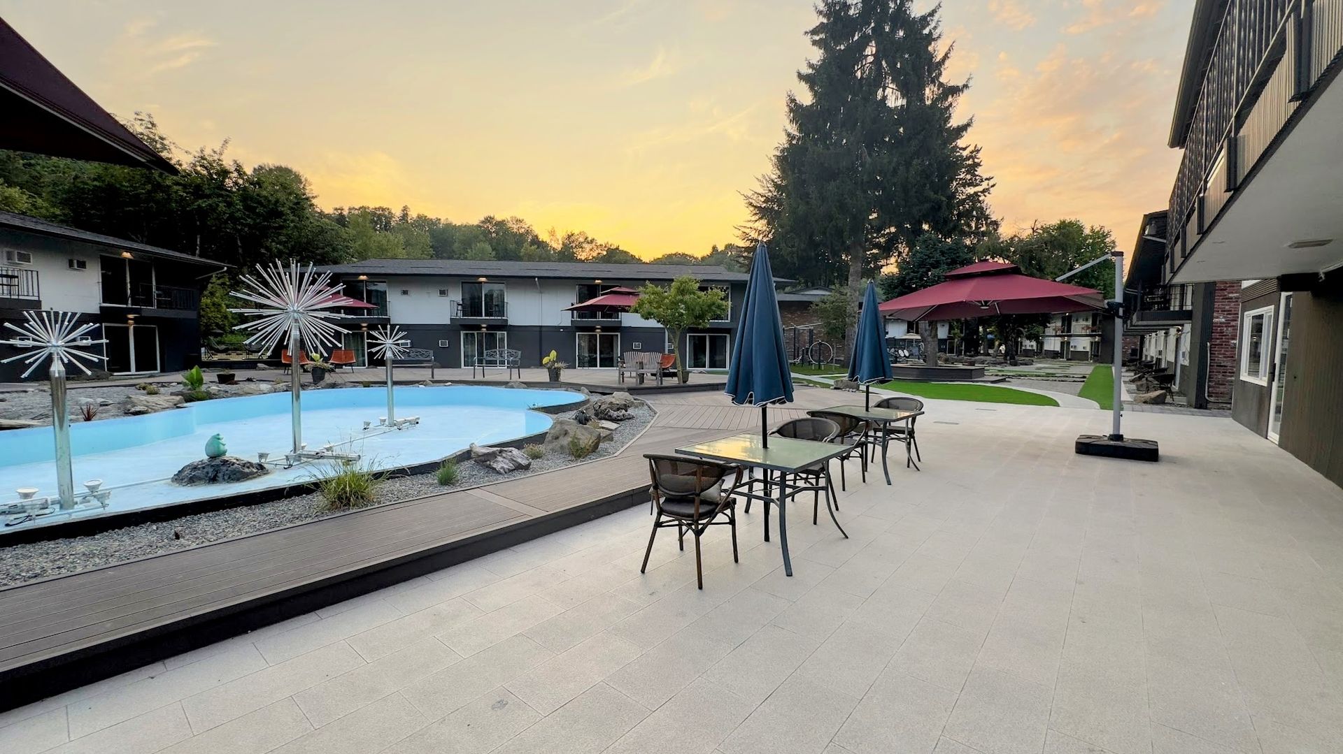A patio with tables and chairs and umbrellas in front of a swimming pool