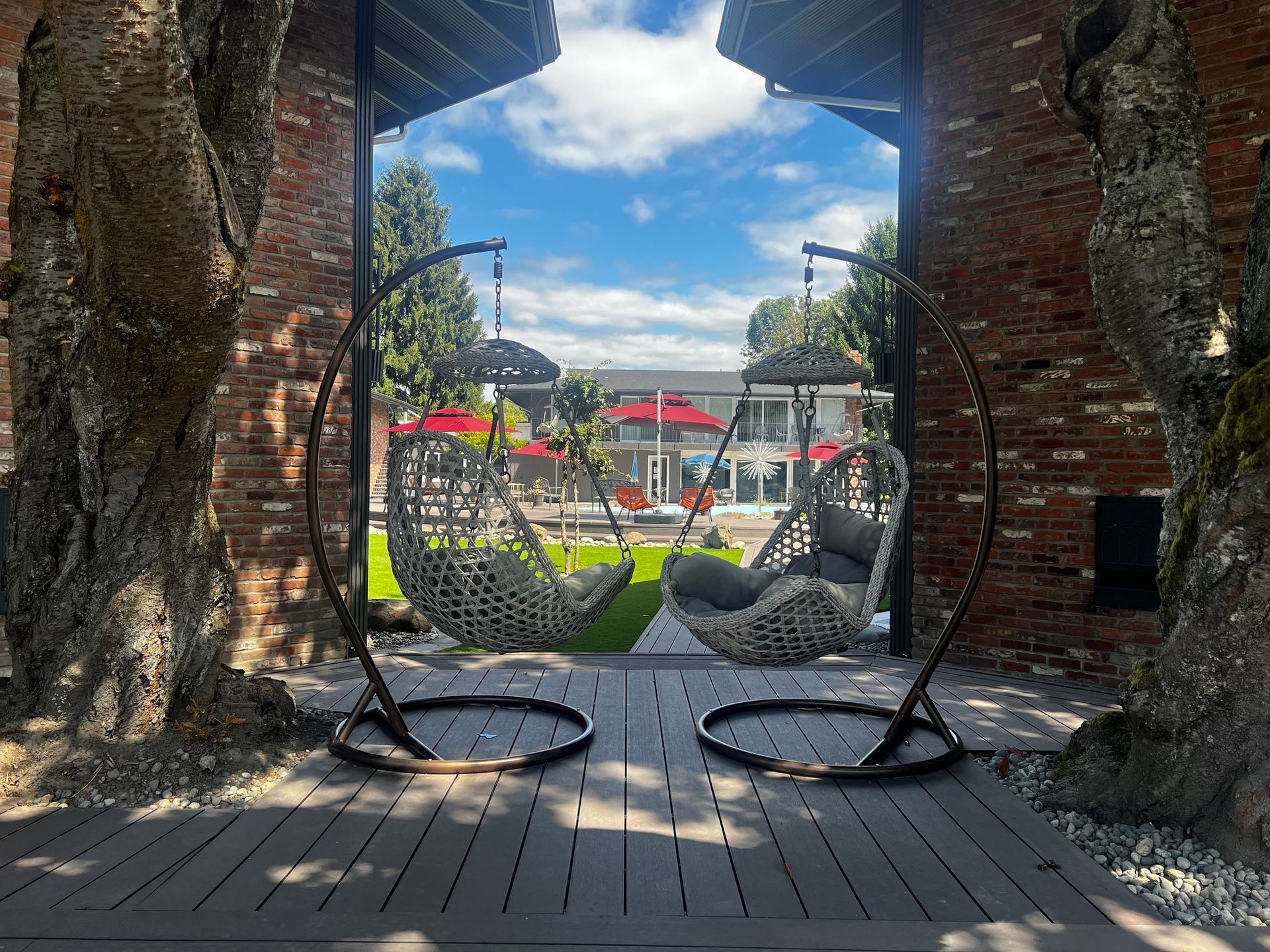 Two hanging chairs are sitting on a wooden deck in front of a brick building.