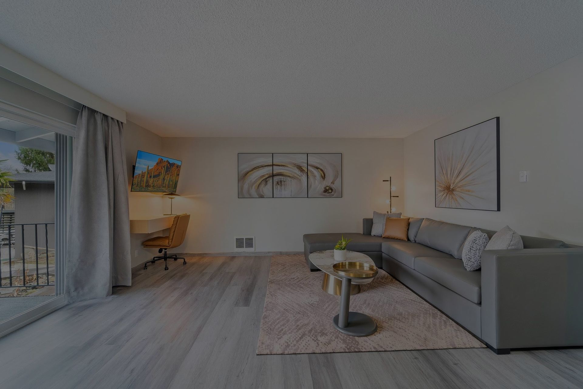 A living room with a couch , coffee table , desk and balcony.