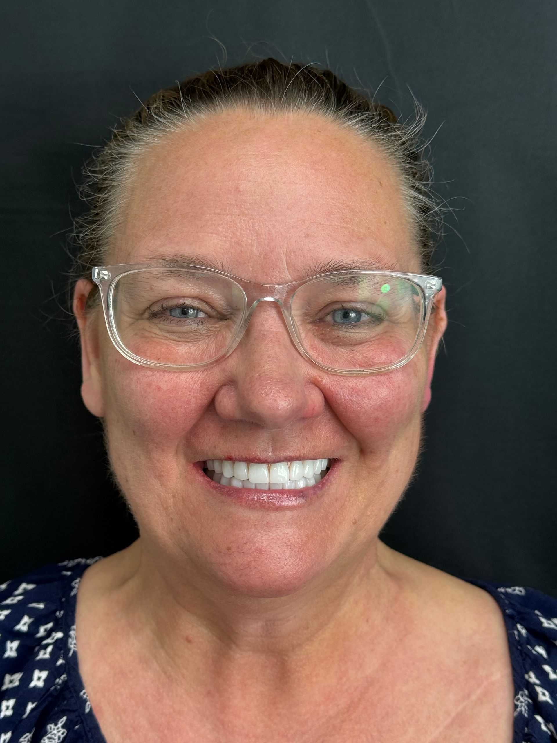 Smiling person wearing clear glasses against a dark background