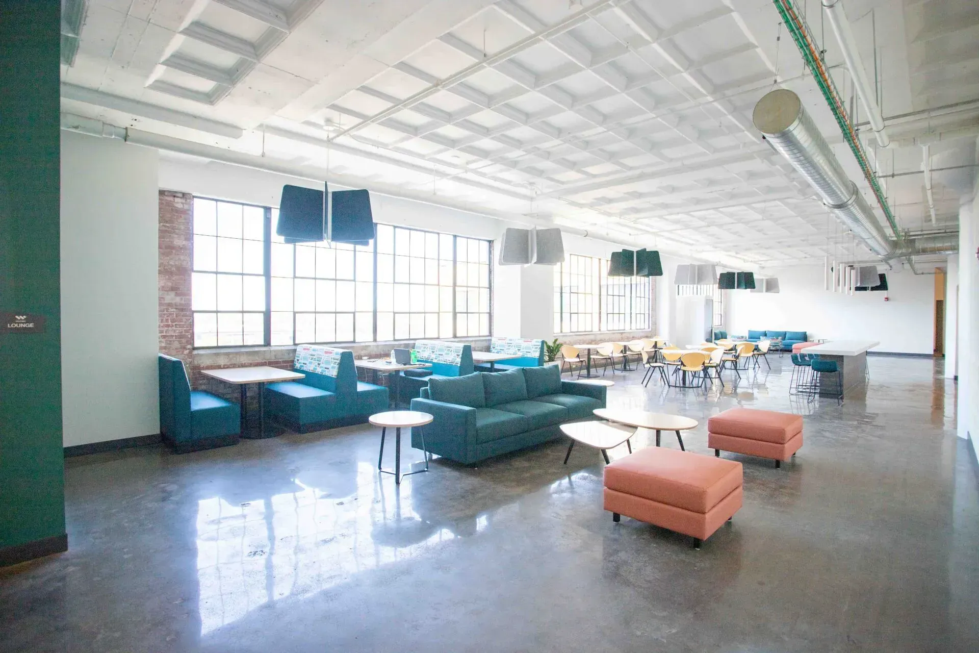 Ample open SCIF office space with teal couches, orange ottomans, and tables by windows.