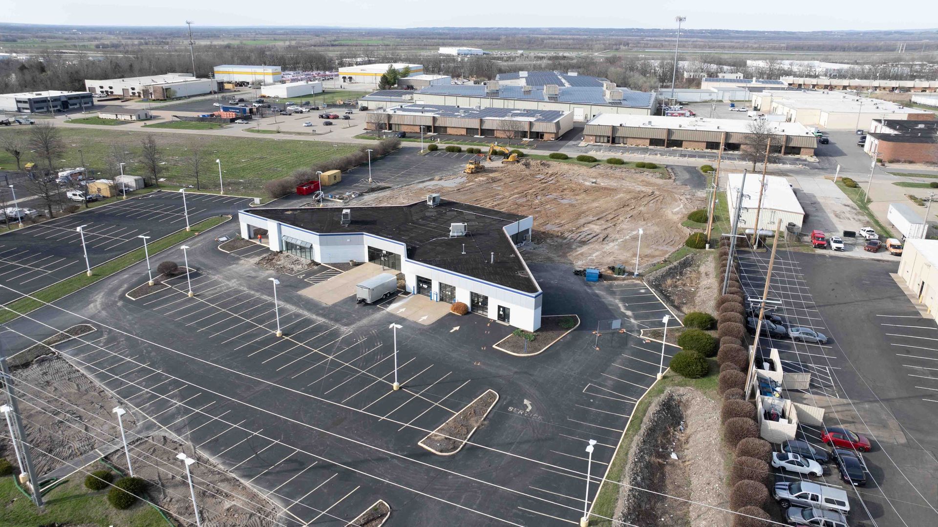 Aerial view of a large commercial building and mostly empty parking lot on a sunny day