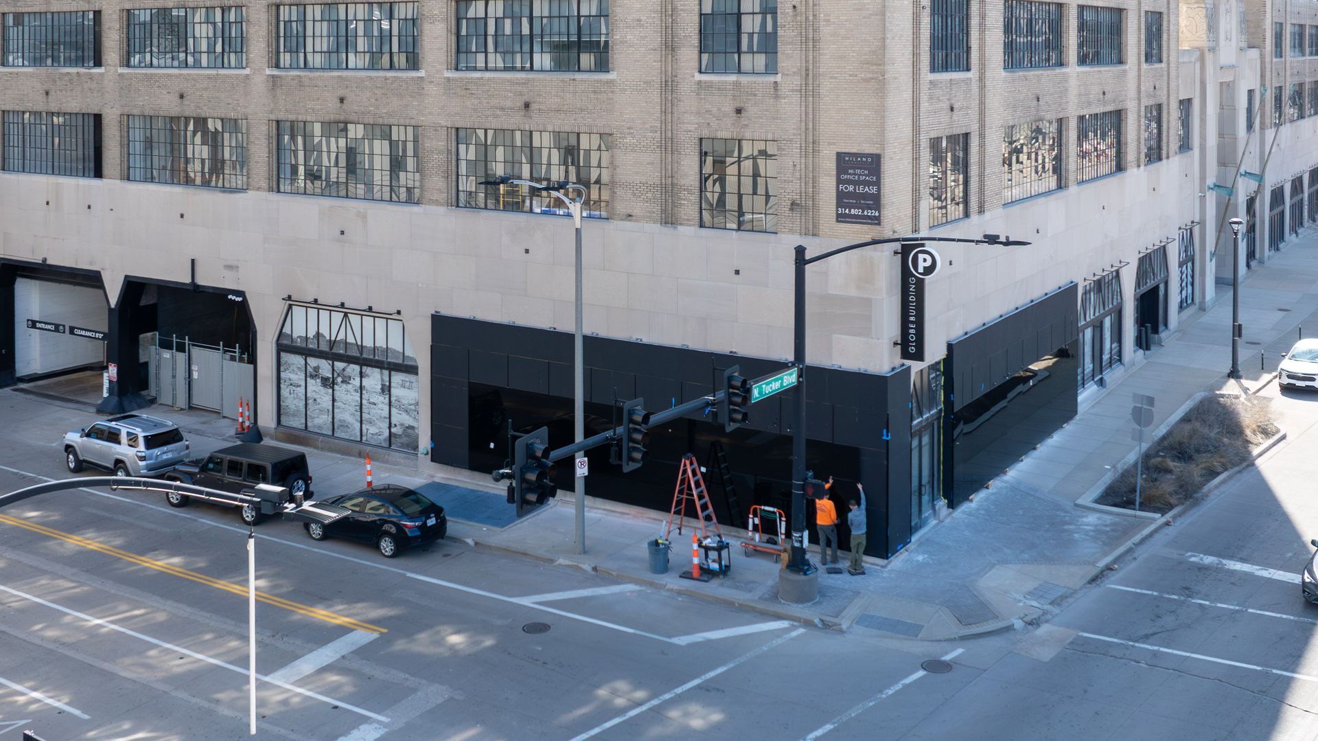 Corner building with black facade and white trim. Cars parked on street, traffic light.
