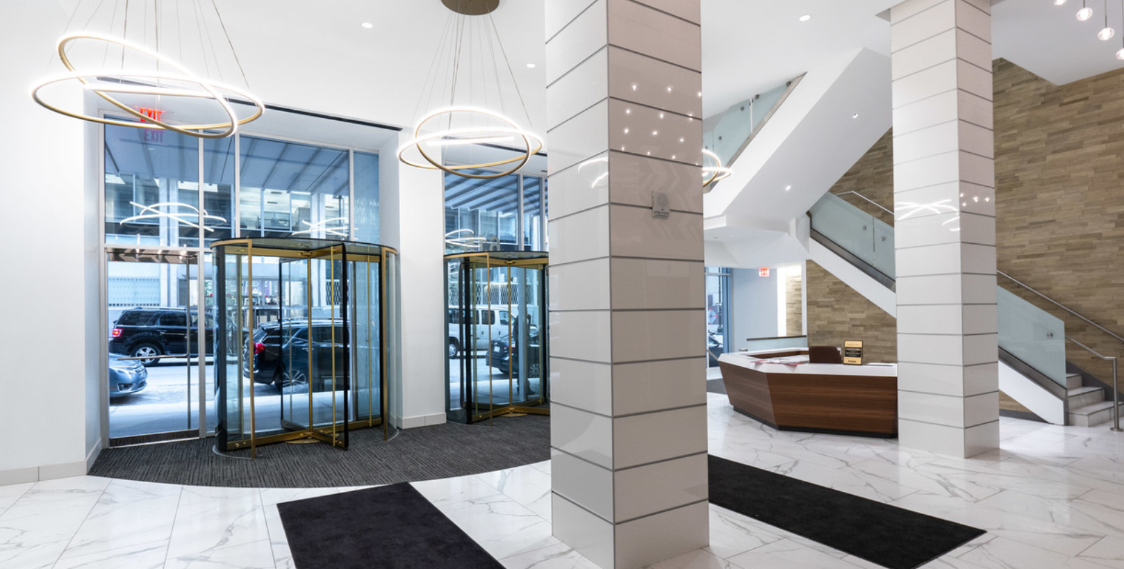 Modern building lobby with revolving doors, marble floor, and staircase.