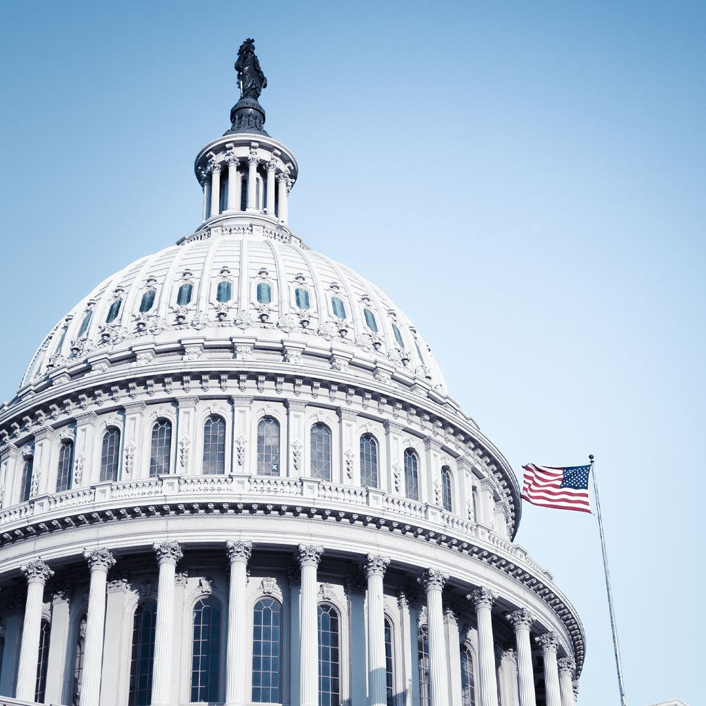 United States Capitol Building with American flag in front of a blue sky.