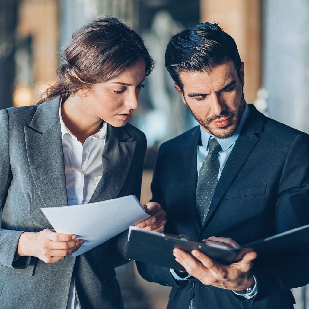 Two professionals, a man and a woman, reviewing documents in an office setting.