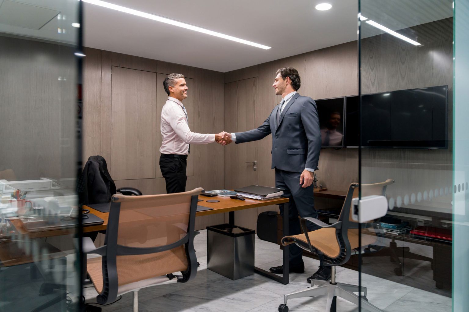 Two people shaking hands in an office, smiling.