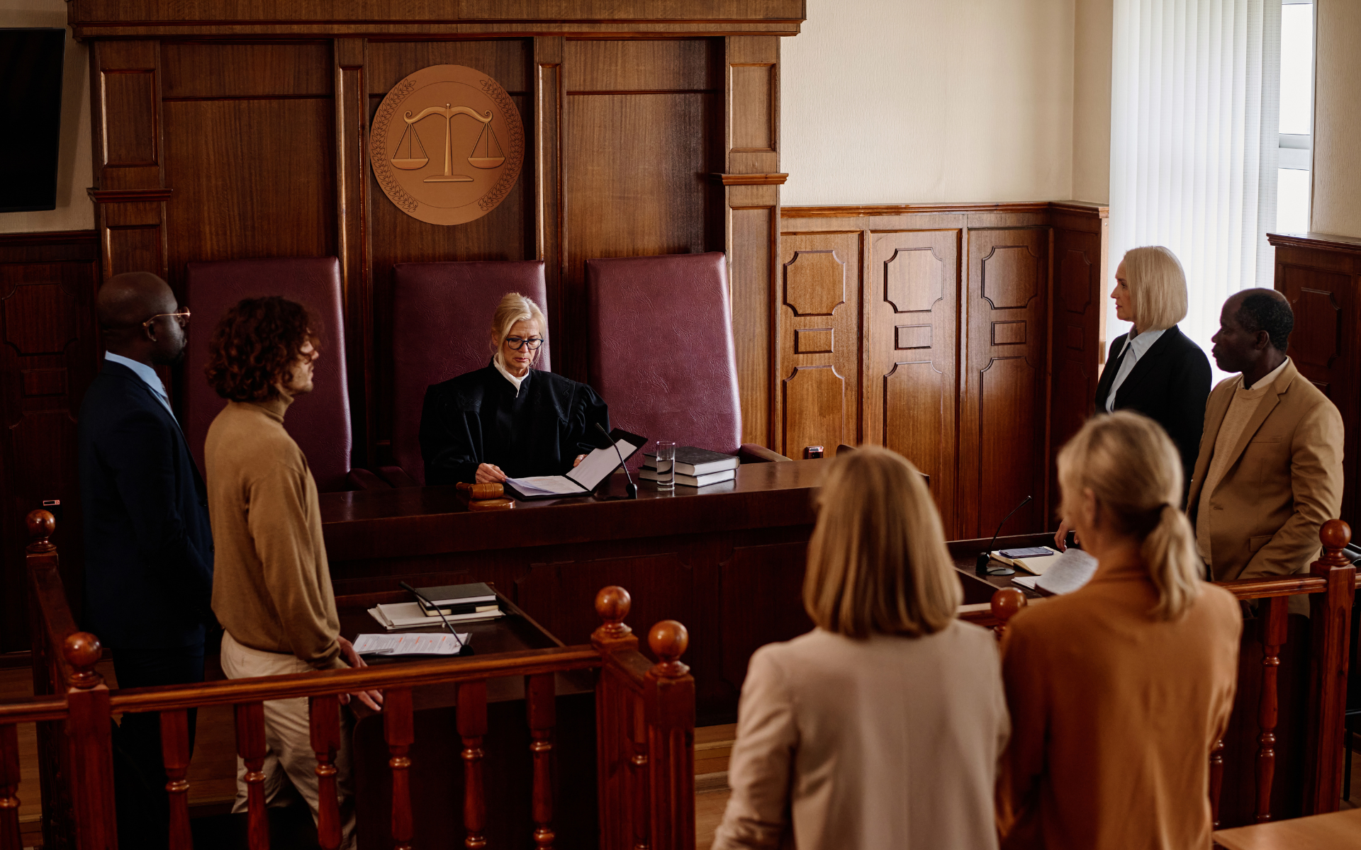 Courtroom scene: Judge in the center, lawyers and people standing, with wooden walls and judge's bench.