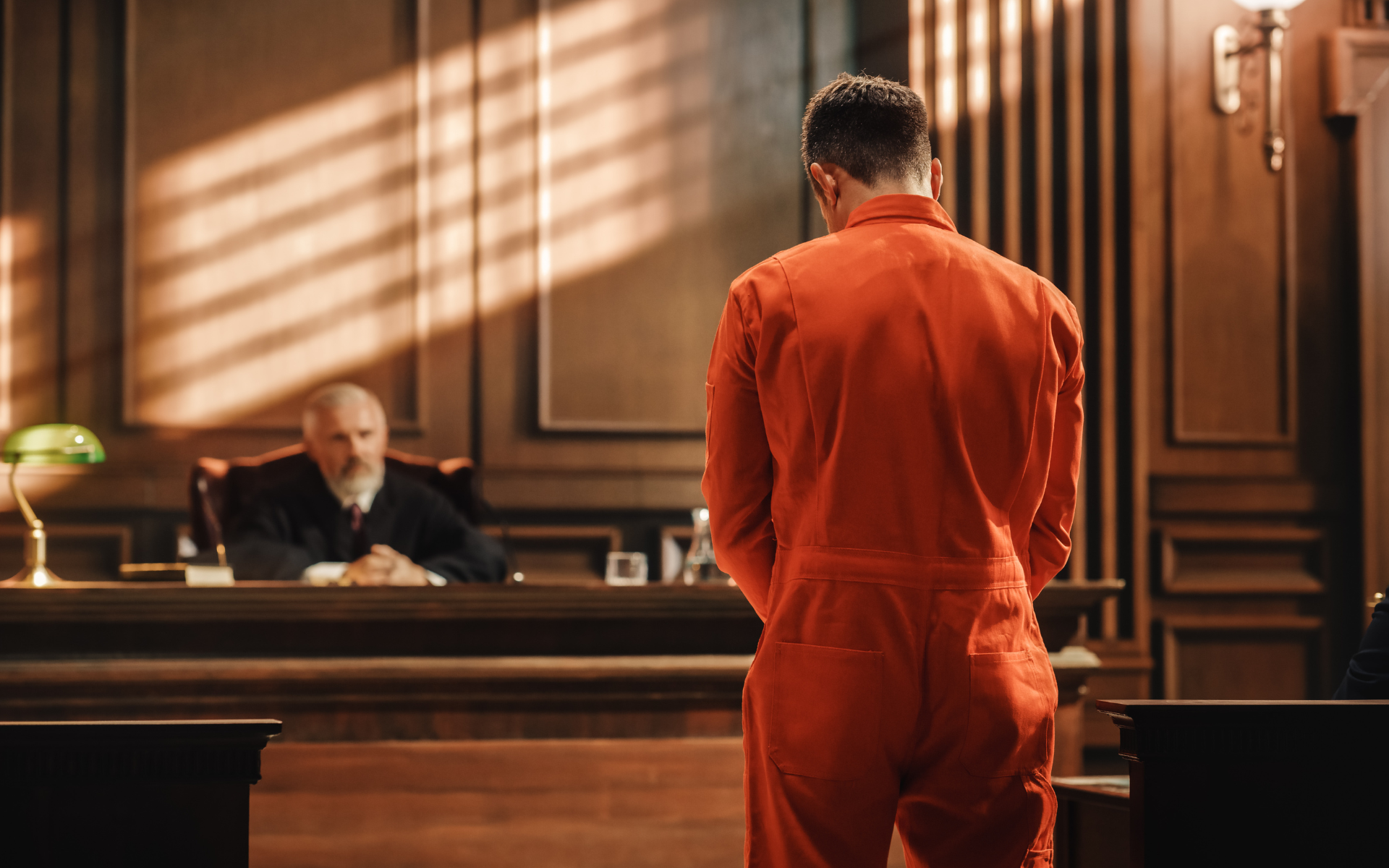 Person in orange jumpsuit stands before a judge in a courtroom.