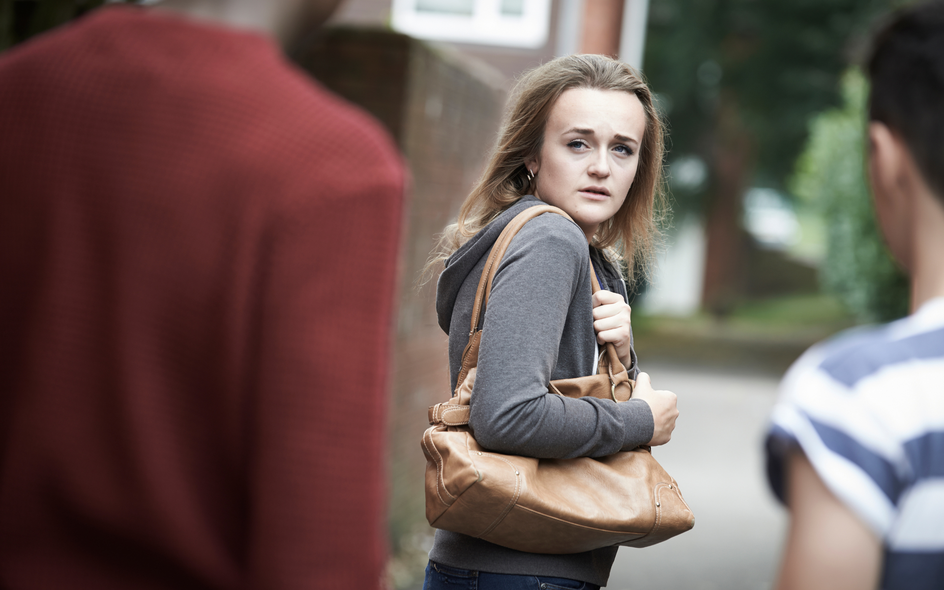 Woman looking back, scared, clutching purse; two people in the background, one in a red shirt.