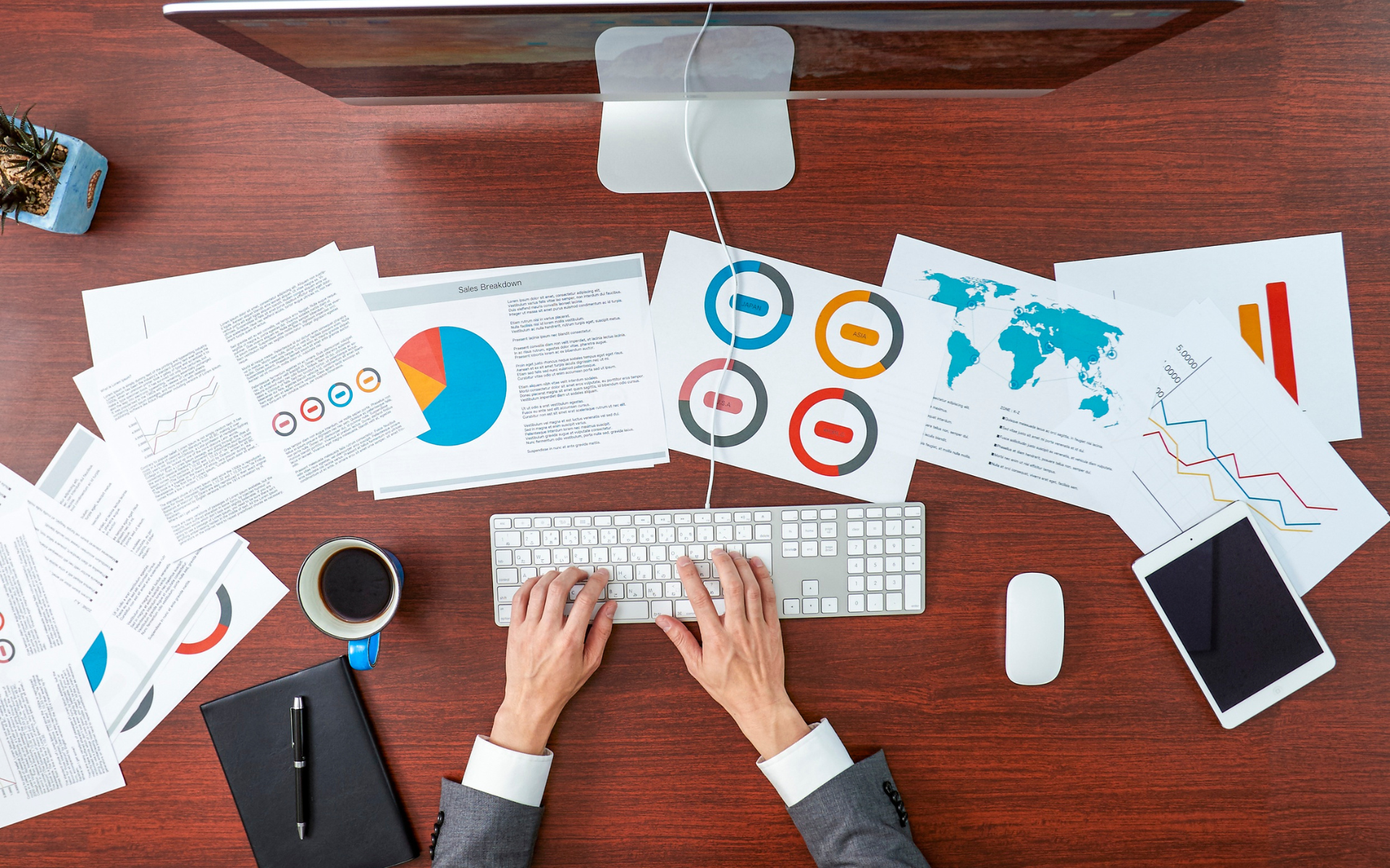 Person typing at a desk surrounded by financial charts and a computer.