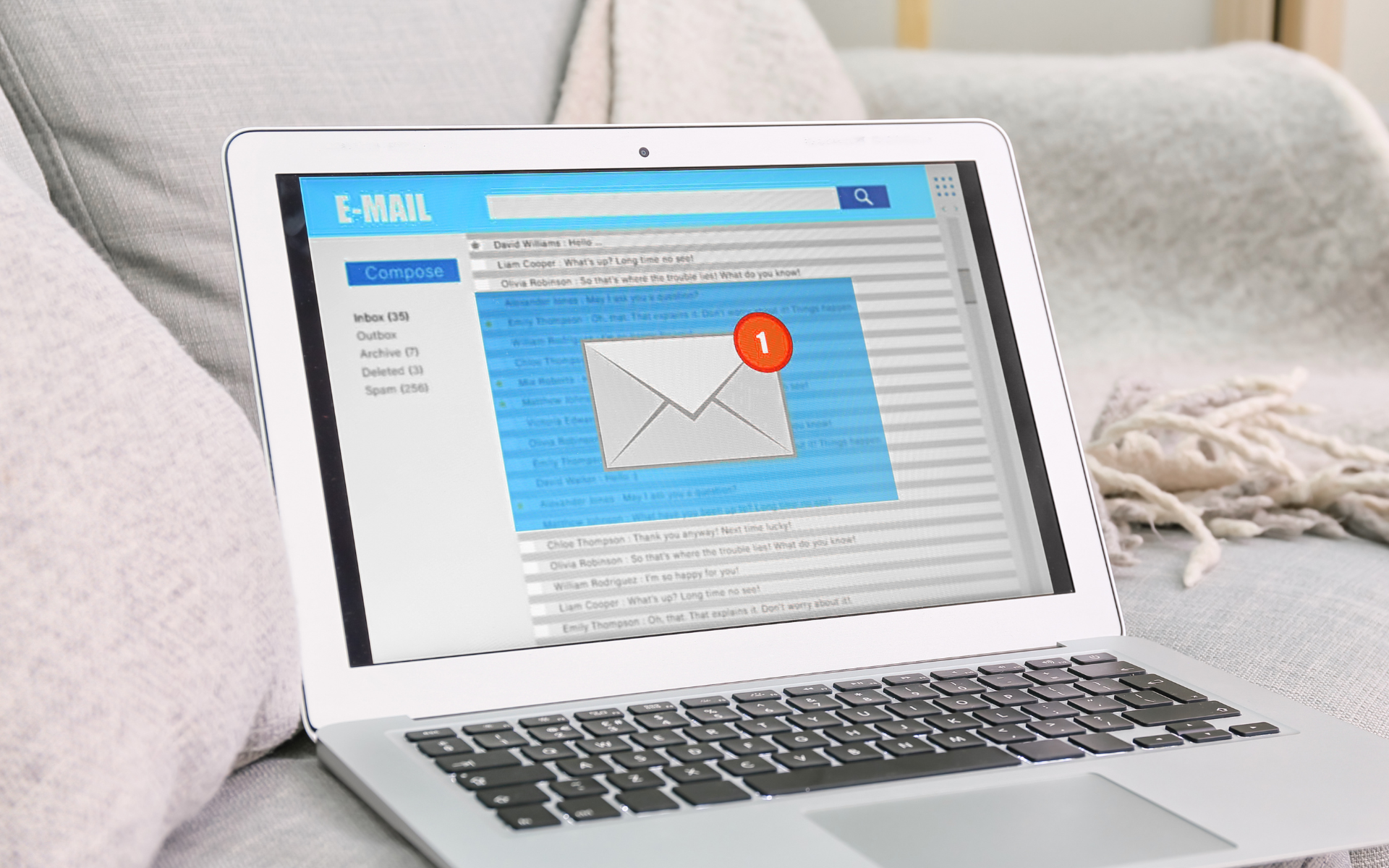 Laptop on a couch displaying an email inbox, with an unread message indicated by a red notification.