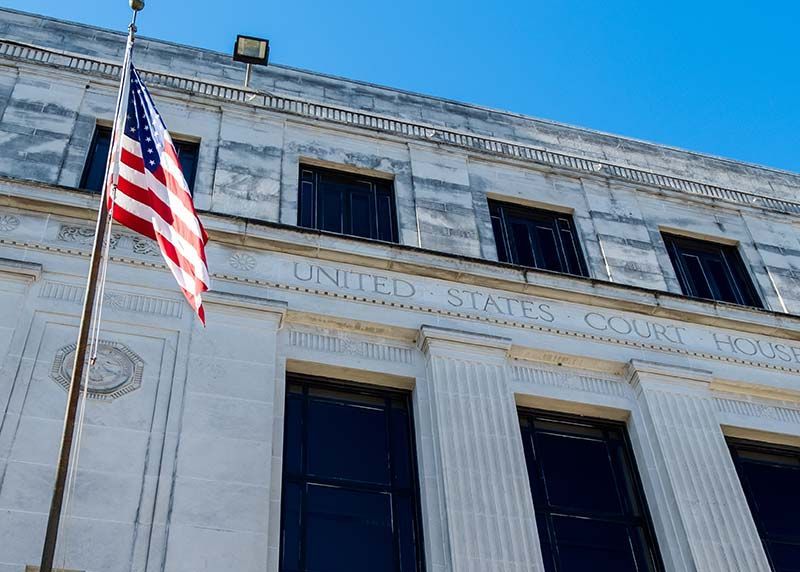 American flag flying in front of a United States Courthouse on a sunny day.