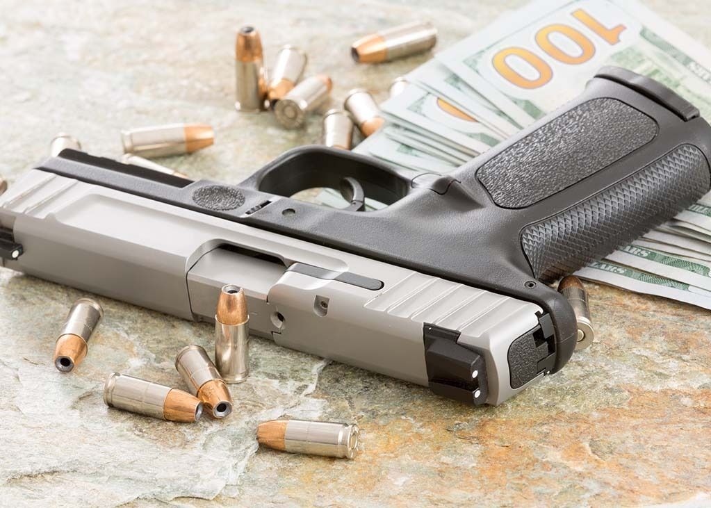 Handgun with bullets and money on a textured surface.