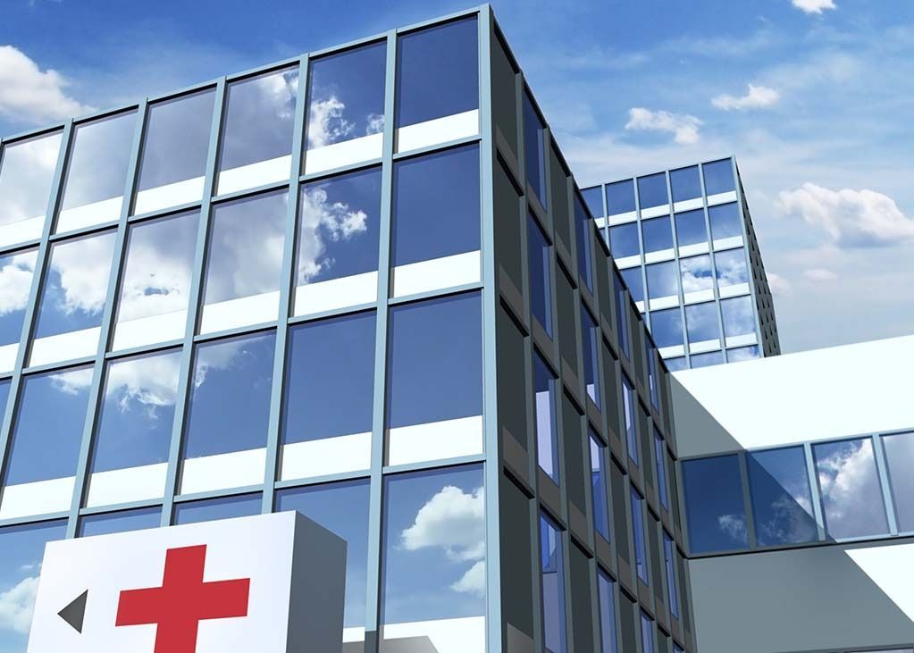 Hospital building with glass windows and a red cross symbol. Blue sky with clouds.