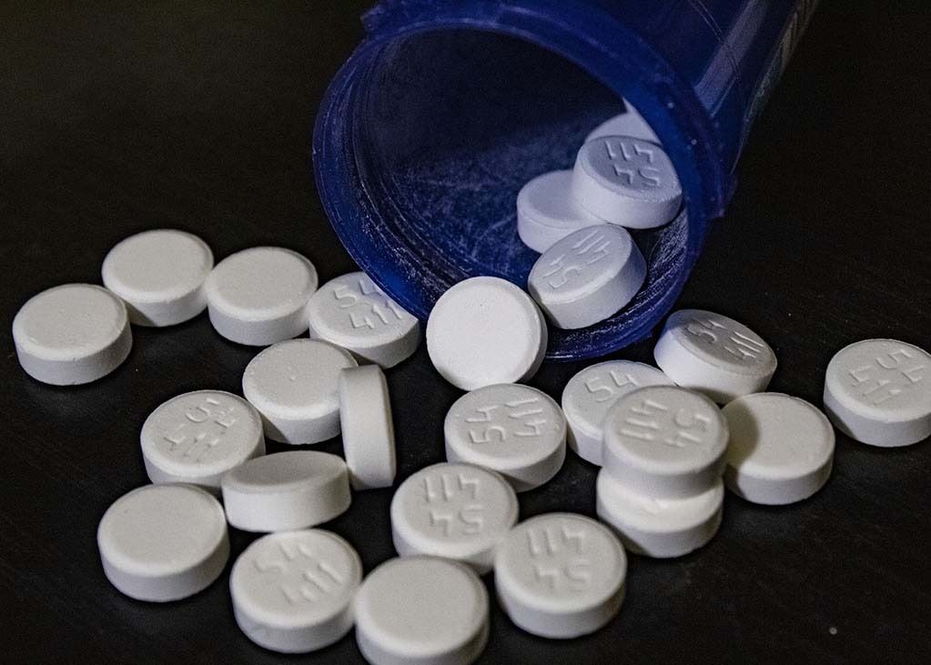 White pills spilling from a blue prescription bottle on a dark surface.