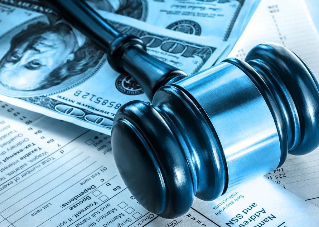 Gavel on tax forms and US currency, symbolizing legal and financial matters.