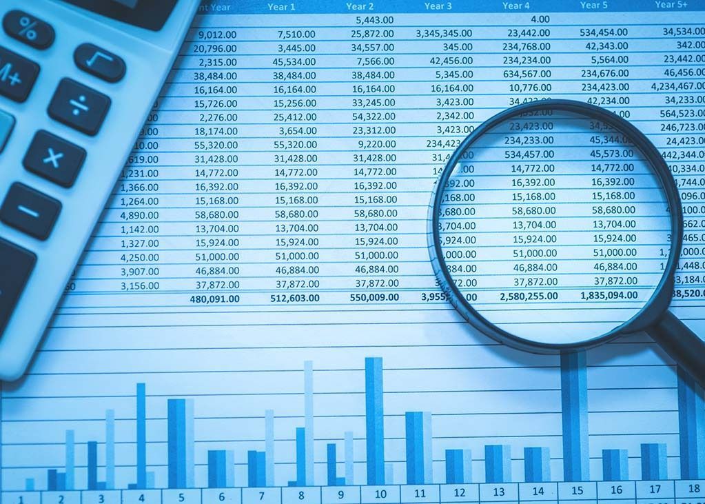 Calculator and magnifying glass on financial documents and a bar graph.