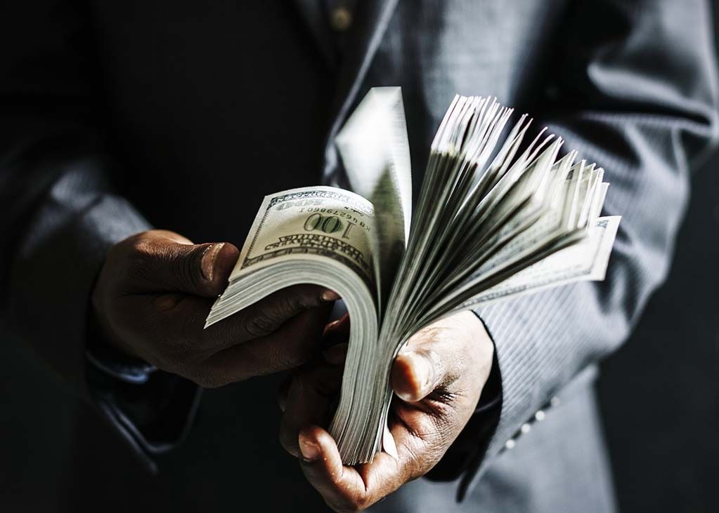 Person in suit holding a large stack of US dollar bills.