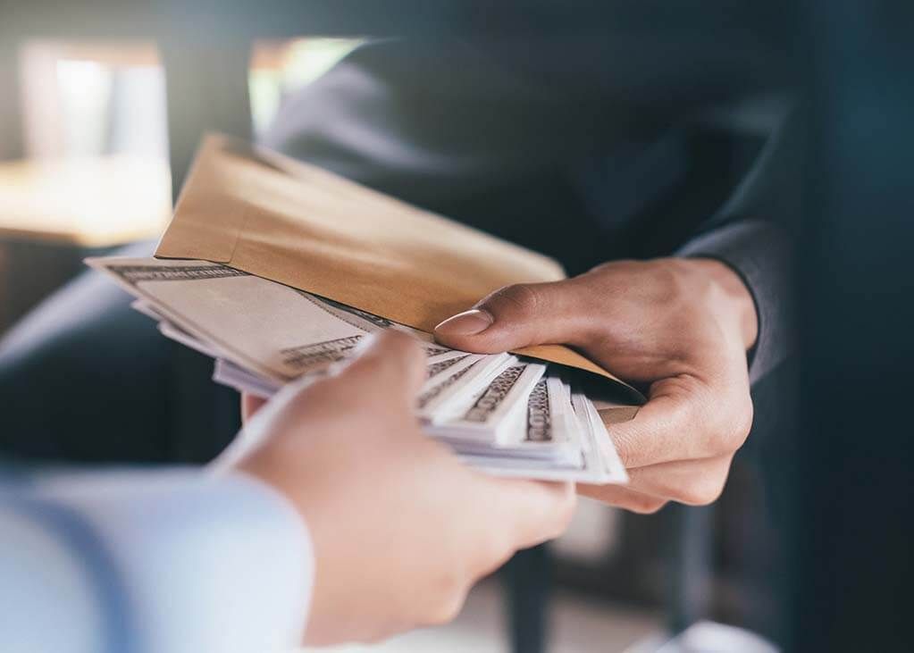 Hands exchanging money from an envelope, suggesting bribery or an illicit transaction.