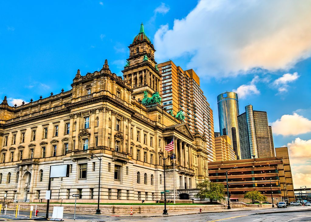 A large, ornate building with a tall tower next to modern skyscrapers under a blue sky.