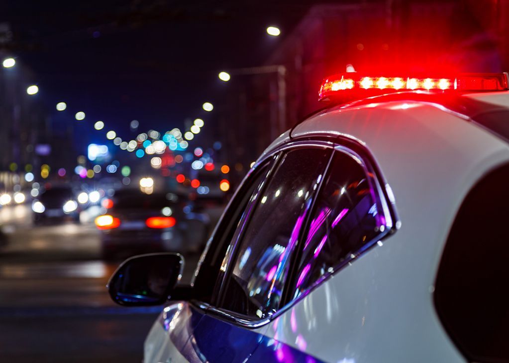 Police car with flashing red lights on a city street at night; other vehicles blurred in the background.