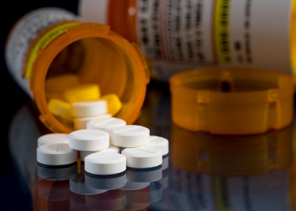 Pills spilling from orange prescription bottles on a reflective surface.