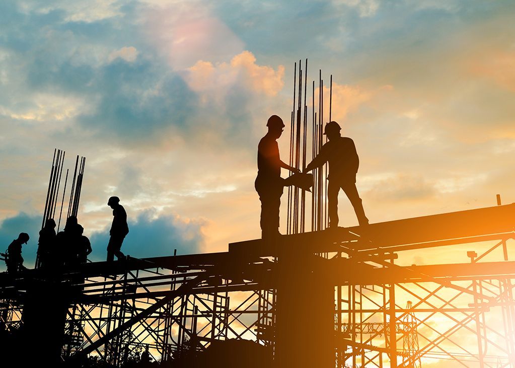 Construction workers silhouetted on a building site at sunset, working on the framework.
