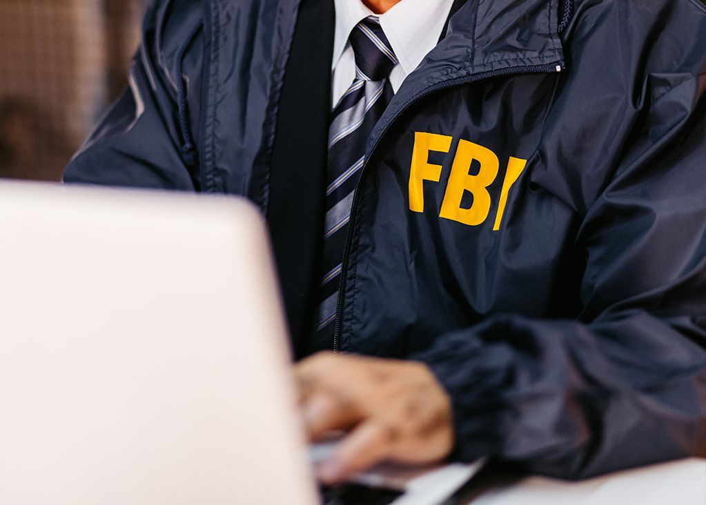 FBI agent in navy jacket with yellow letters, using a laptop.