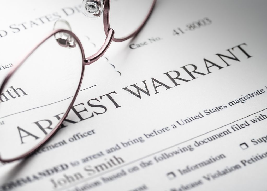 Arrest warrant document with glasses resting on it, including the name 