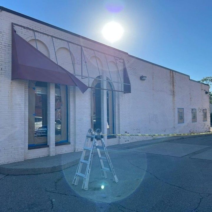 A white building with a red awning and a ladder in front of it