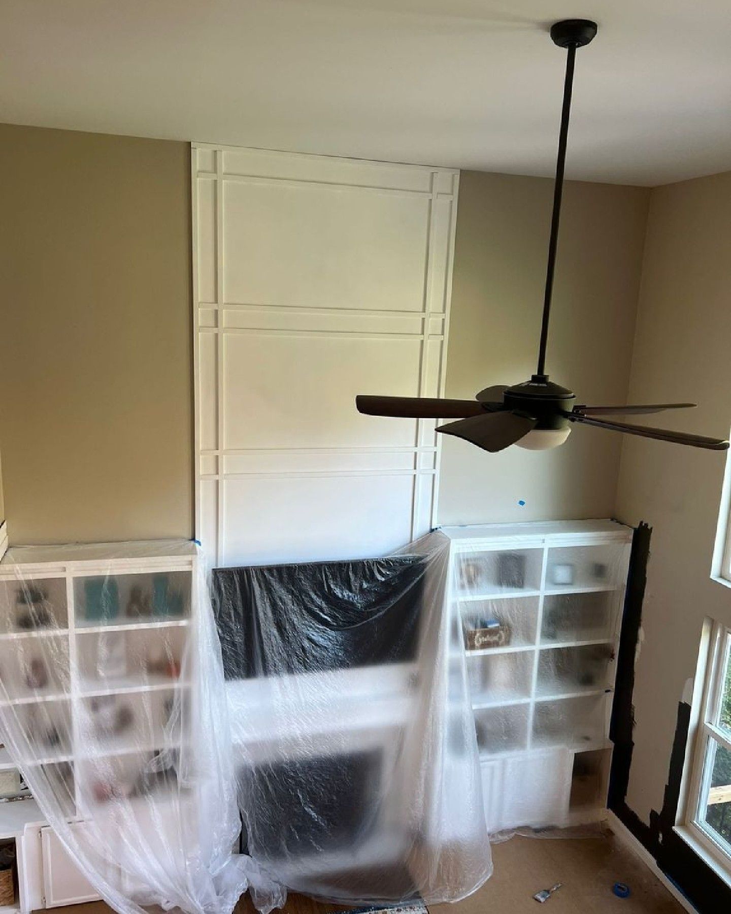A living room with a fireplace covered in plastic and a ceiling fan.