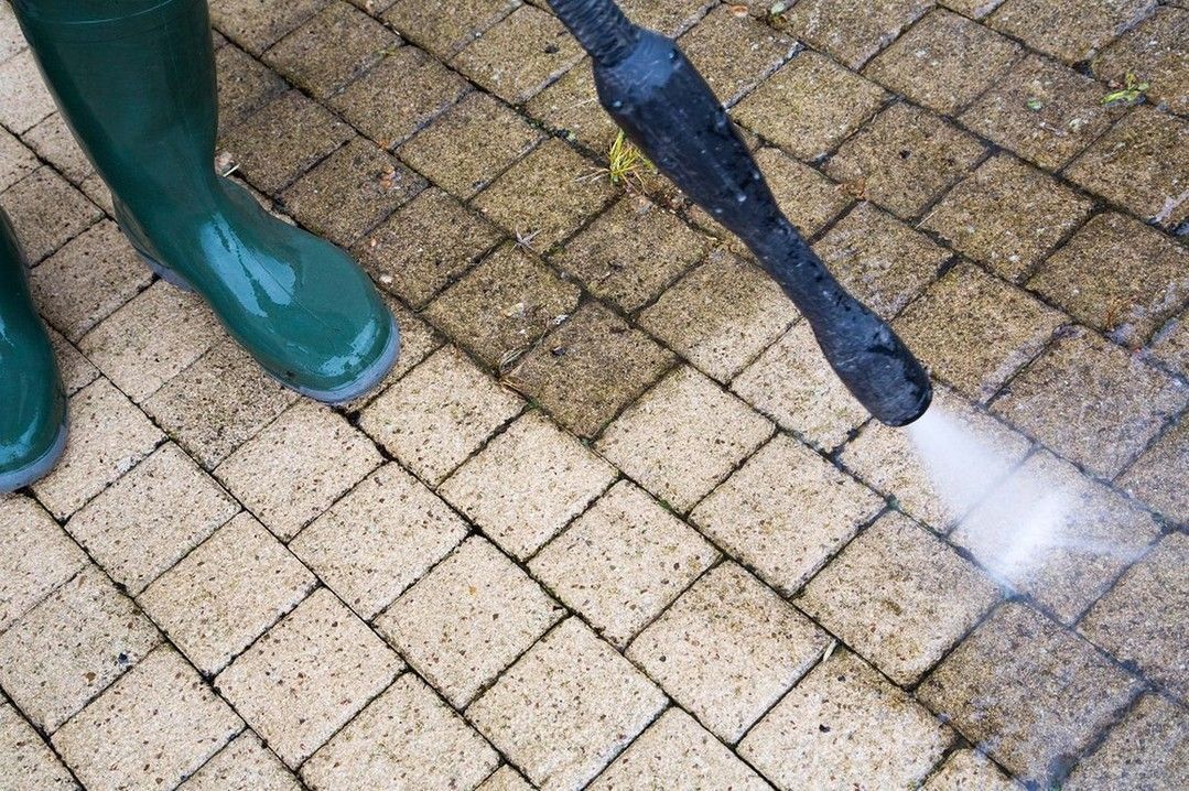 A person is using a high pressure washer to clean a brick walkway.