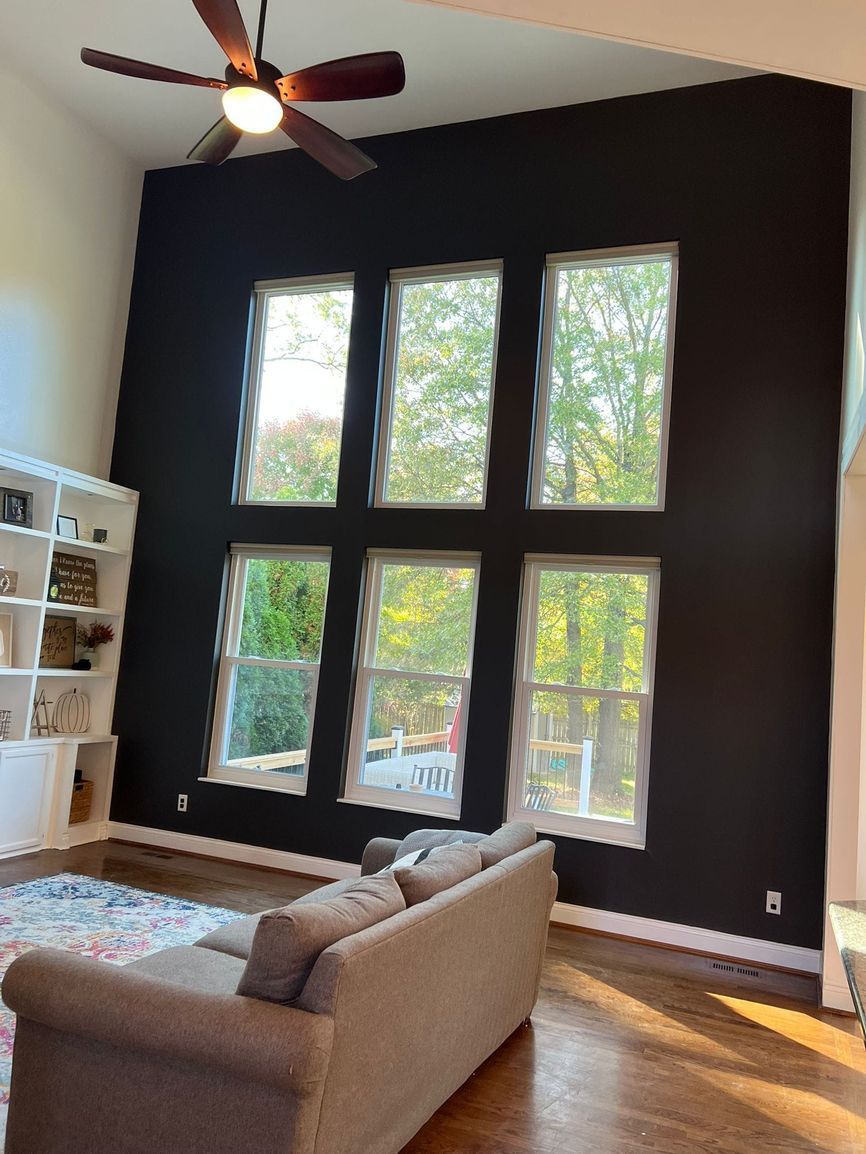 A living room with a couch , ceiling fan , and lots of windows.