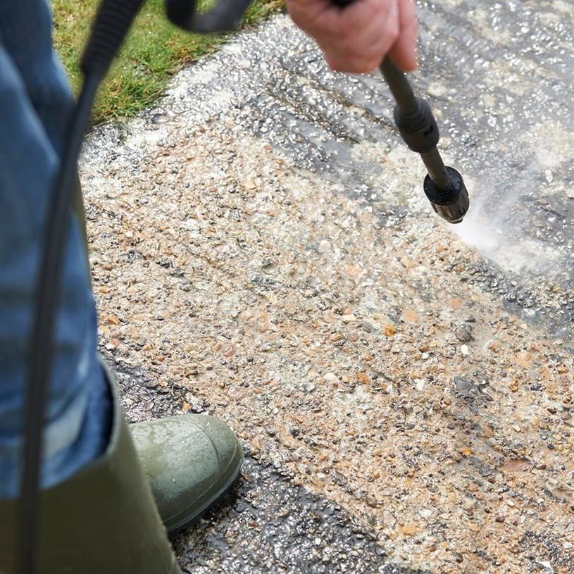 A person is using a high pressure washer to clean a sidewalk