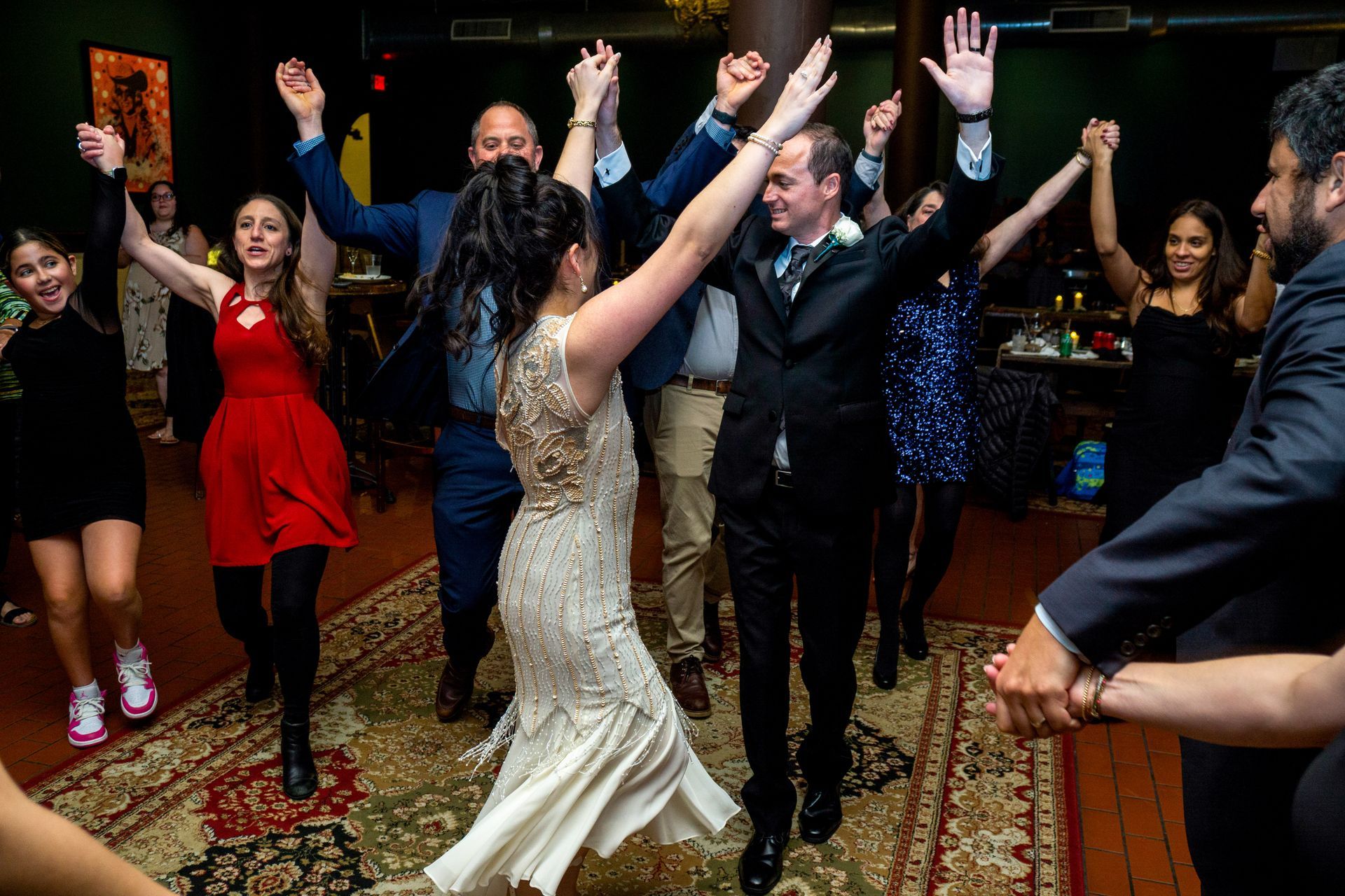 People dancing at a lively indoor party, with arms raised and festive outfits.